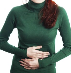 Woman wearing a green turtle neck holding her stomach due to pain